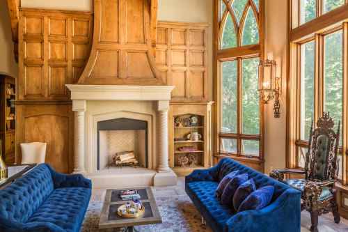 Cozy living room with a stone fireplace, wooden paneling, large windows, and elegant blue sofas.