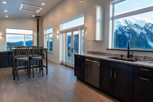 Modern kitchen with a view of mountains, featuring a sink, dark cabinets, and a dining area with tall chairs.