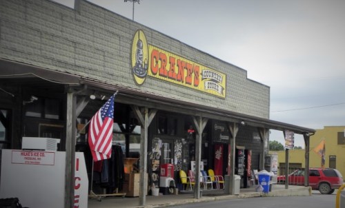 A rustic storefront with a large sign reading "Country Store," featuring an American flag and outdoor seating.