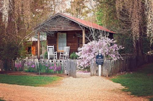 A rustic wooden cabin with a red roof, surrounded by blooming flowers and a picket fence, inviting rocking chairs on the porch.