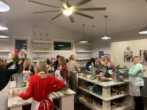 A group of people in an indoor space arranging flowers at a workshop, surrounded by floral supplies and decor.