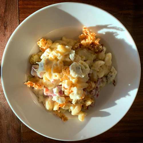 A bowl of creamy pasta topped with crispy onions and bits of ham, served on a wooden table.