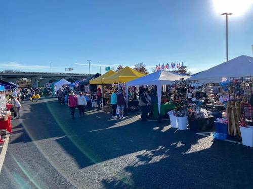 A bustling outdoor market with colorful tents, vendors, and shoppers under a clear blue sky.