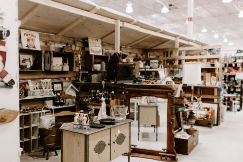 A vintage shop interior featuring wooden shelves, antique items, and a rustic table with various collectibles.