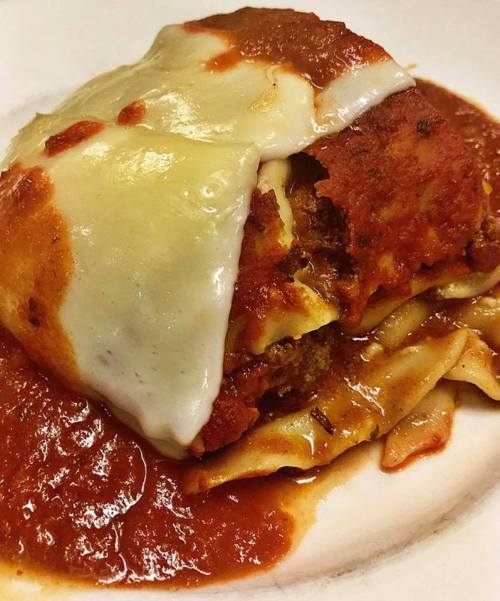 A serving of lasagna topped with melted cheese and marinara sauce on a white plate.