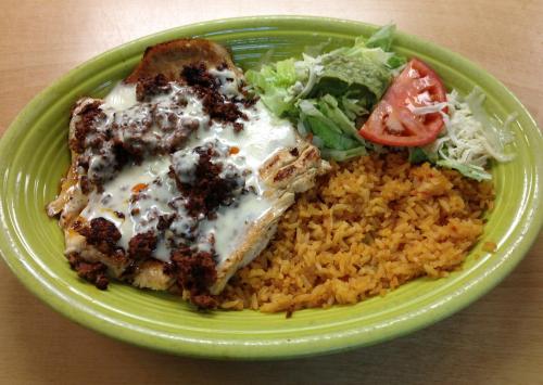 A vibrant plate of chicken topped with sauce, served with rice, lettuce, tomato, and cheese on a green dish.