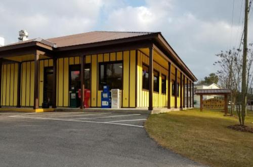 A yellow and brown restaurant building with large windows and a sign, set in a grassy area under a cloudy sky.