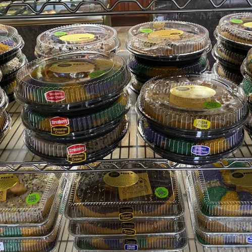 A display of various cakes in clear plastic containers, stacked on shelves with colorful labels.