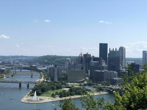 A panoramic view of Pittsburgh's skyline, featuring bridges and the river, under a clear blue sky.