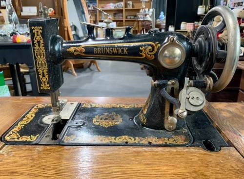 Antique Brunswick sewing machine with ornate detailing, set on a wooden table in a vintage shop.