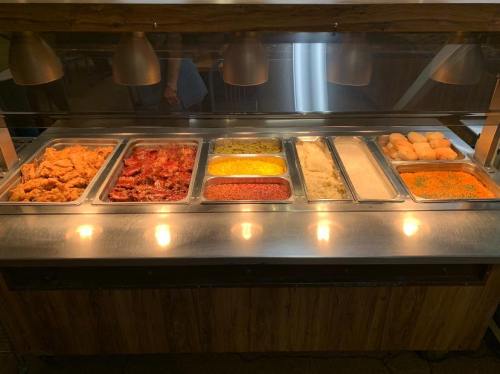 A buffet display featuring various trays of fried chicken, pasta, rice, and rolls under warm lighting.