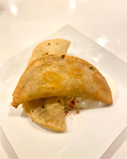 A plate with two golden-brown empanadas and a dollop of creamy sauce, garnished with a sprinkle of spice.