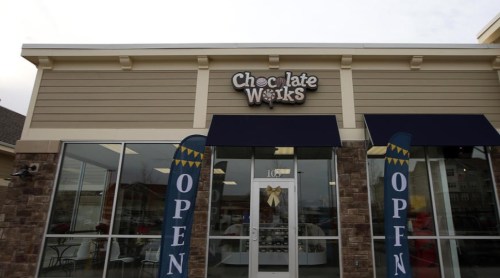 Exterior of a Chocolate Works store with "OPEN" signs and a festive bow on the entrance.