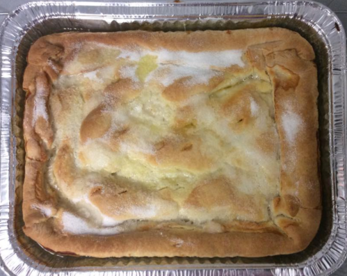 A golden-brown baked dessert in a silver tray, lightly dusted with sugar on top.