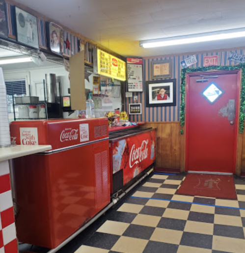 A retro diner interior featuring a Coca-Cola fridge, checkered floor, and a red exit door decorated for the holidays.