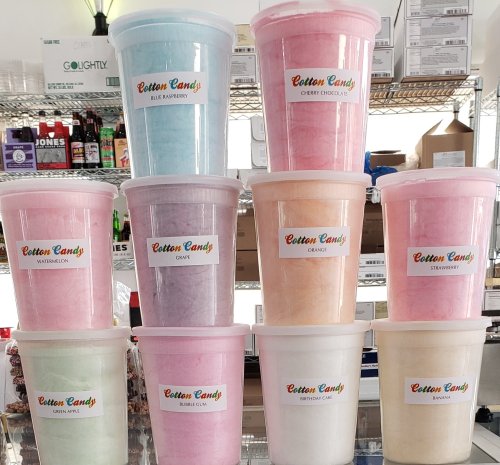 A stack of colorful cotton candy tubs labeled with flavors like watermelon, blue raspberry, and strawberry.