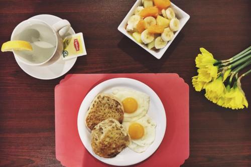 A plate with two fried eggs and biscuits, a bowl of mixed fruit, a cup of tea with lemon, and yellow flowers.