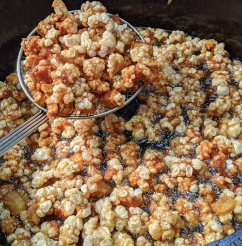A metal strainer lifting crispy, golden popcorn from a pot of hot oil.