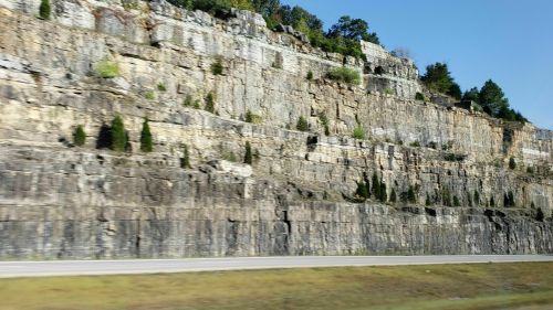 A rocky cliffside with layered stone formations and sparse greenery under a clear blue sky.