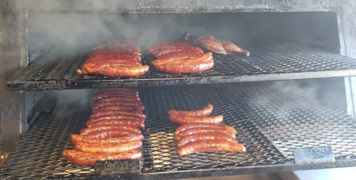 Smoky barbecue sausages and a piece of meat on a grill, with steam rising from the cooking surface.