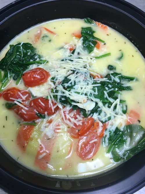 A bowl of creamy soup with spinach, cherry tomatoes, and grated cheese on top.