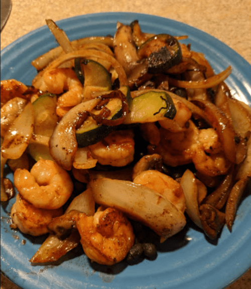 A blue plate filled with sautéed shrimp, zucchini, onions, and mushrooms.