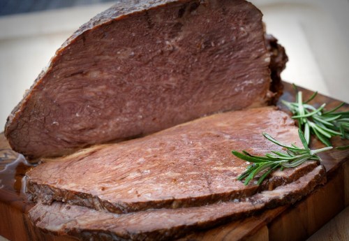 Sliced roast beef on a wooden cutting board, garnished with fresh rosemary.