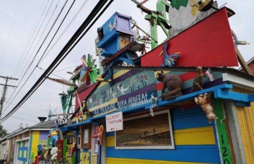 Colorful, whimsical building adorned with various sculptures and decorations, set against a cloudy sky.