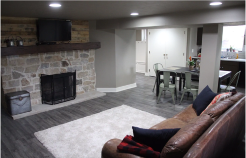 Cozy living space with a stone fireplace, TV, and a dining area featuring a table and chairs. Soft rug and leather sofa.