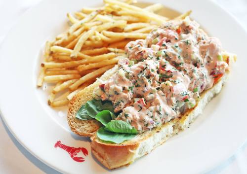 A lobster roll topped with creamy lobster salad on a toasted bun, served with a side of crispy French fries.