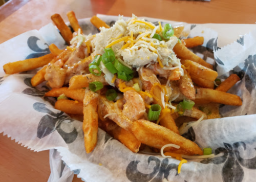 A plate of loaded fries topped with cheese, green onions, and shredded chicken, served in a basket.