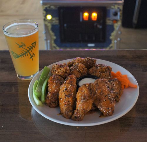 A plate of chicken wings with celery and carrots, served with a dipping sauce, alongside a glass of beer.