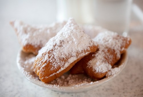 A plate of powdered sugar-dusted beignets, with a glass of water in the background.