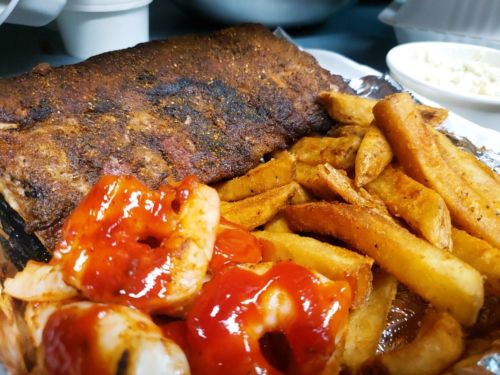 A plate featuring grilled ribs, crispy fries, and shrimp drizzled with red sauce.
