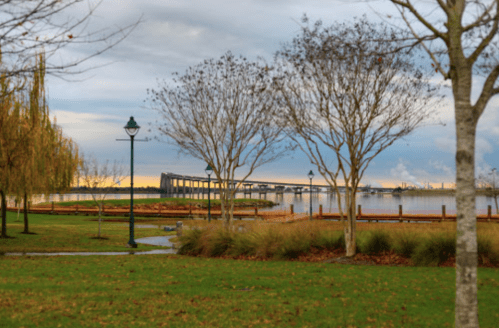 A serene waterfront scene with trees, a bridge in the distance, and a cloudy sky reflecting on the water.