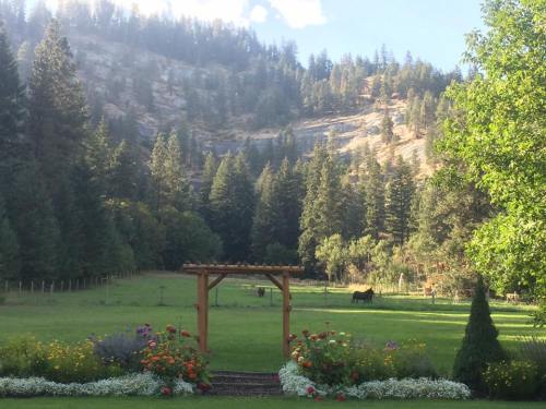 A scenic landscape featuring a wooden arch, colorful flowers, and horses grazing in a lush green field surrounded by trees.