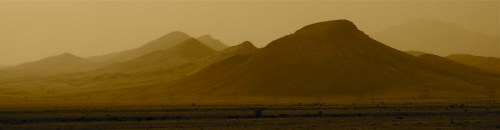 Silhouetted mountains in a golden desert landscape under a hazy sky.
