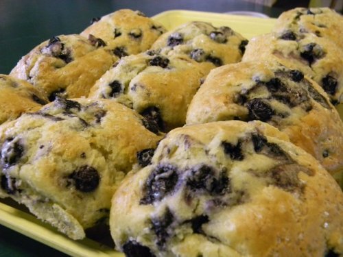 A close-up of freshly baked scones with blueberries, arranged on a yellow tray.