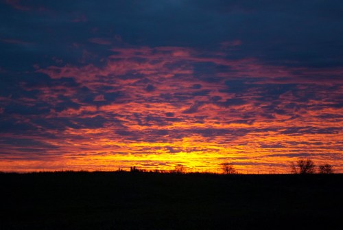 A vibrant sunset with orange and purple hues illuminating the sky over a dark silhouette of a landscape.