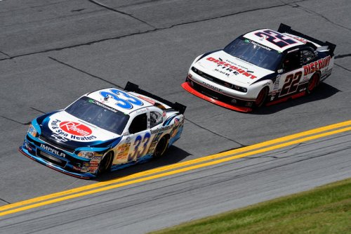 Two NASCAR race cars compete on a track, one blue and white with the number 33, the other black and red with the number 22.