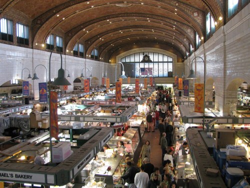 A bustling market interior with vendors, shoppers, and colorful banners under a high arched ceiling.
