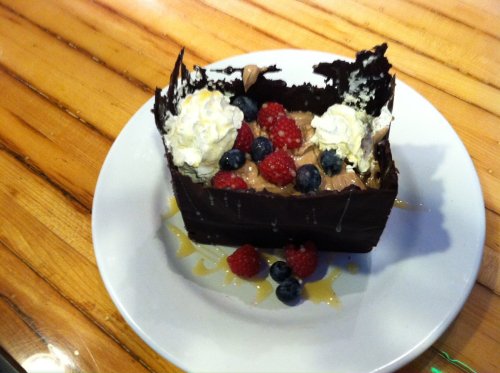 A chocolate dessert bowl filled with mousse, topped with whipped cream and fresh raspberries and blueberries.
