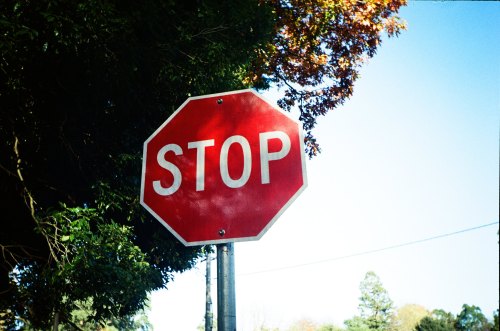 A red octagonal stop sign against a clear blue sky and green foliage.