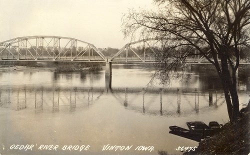 Black and white photo of Cedar River Bridge in Vinton, Iowa, reflecting in the water with trees nearby.
