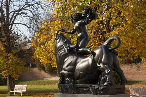 A bronze statue of a woman riding a bull, surrounded by autumn trees with yellow leaves.