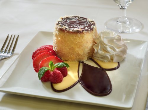 A dessert plate featuring a layered cake, fresh strawberries, raspberries, whipped cream, and chocolate sauce.