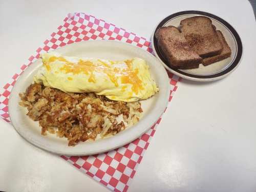 A plate of cheesy omelette with hash browns, accompanied by a side of toasted bread on a checkered napkin.