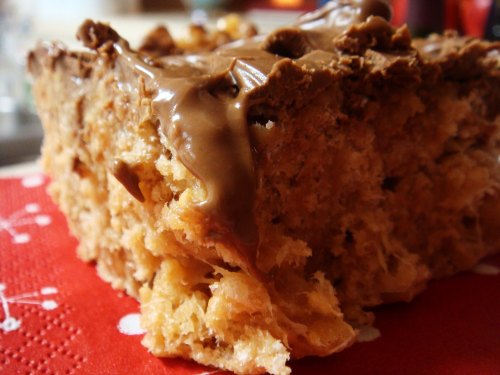 Close-up of a slice of dessert with a crispy base and a smooth chocolate topping, resting on a red napkin.