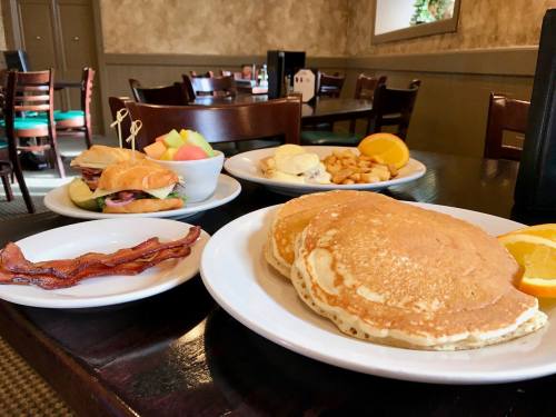 A table set with pancakes, bacon, a sandwich, fruit, and hash browns in a cozy restaurant setting.