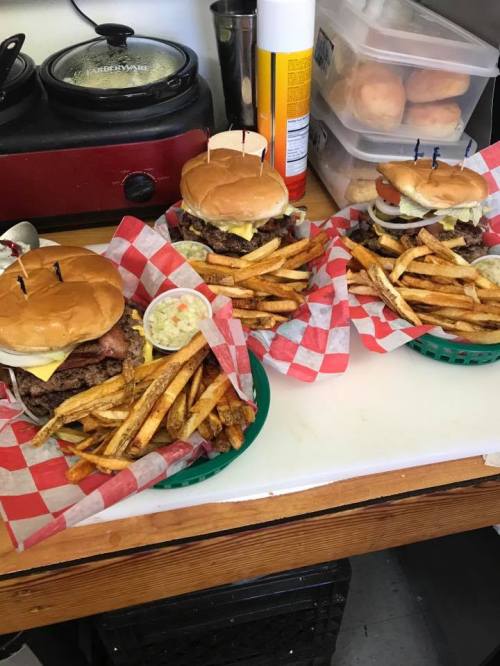 Three baskets of burgers with fries, featuring a variety of toppings, served on a checkered paper.